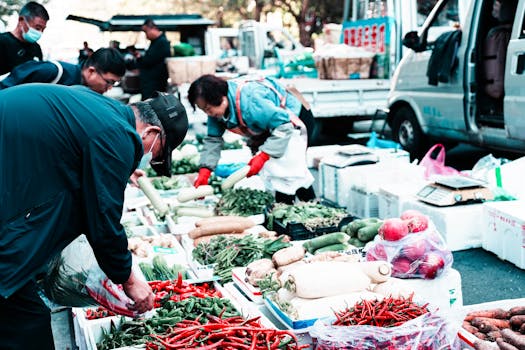 Outdoor market scene with people buying fresh vegetables and produce.