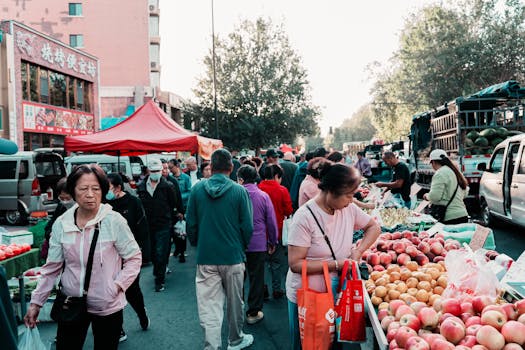 Vibrant outdoor market scene with people buying fresh fruits and vegetables from local vendors.
