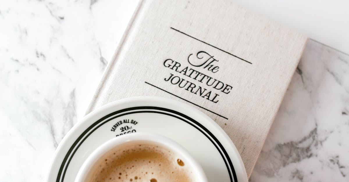 A cup of coffee rests on a gratitude journal against a marble backdrop, capturing peaceful moments.