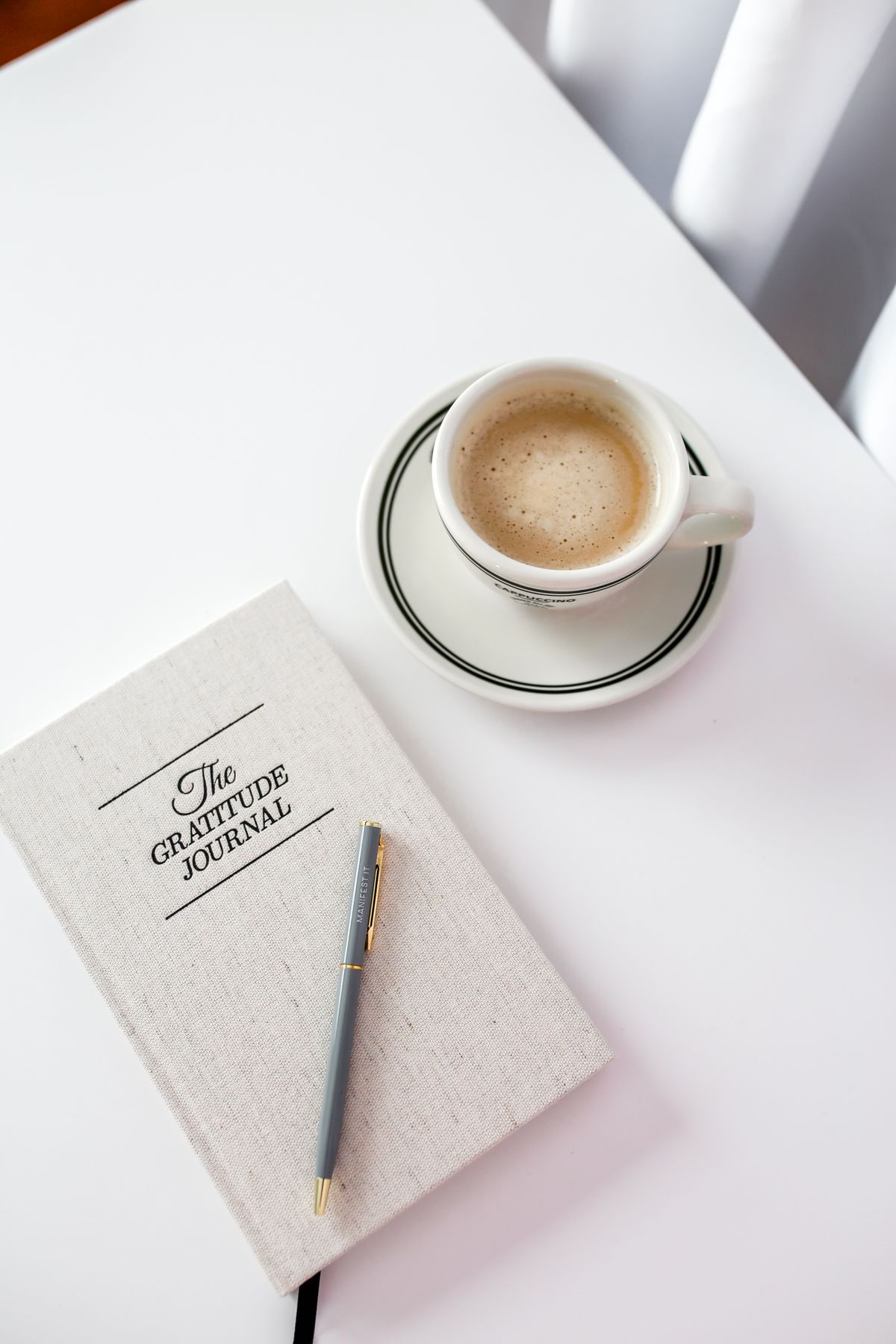 A gratitude journal beside a cup of coffee on a bright, minimalist desk