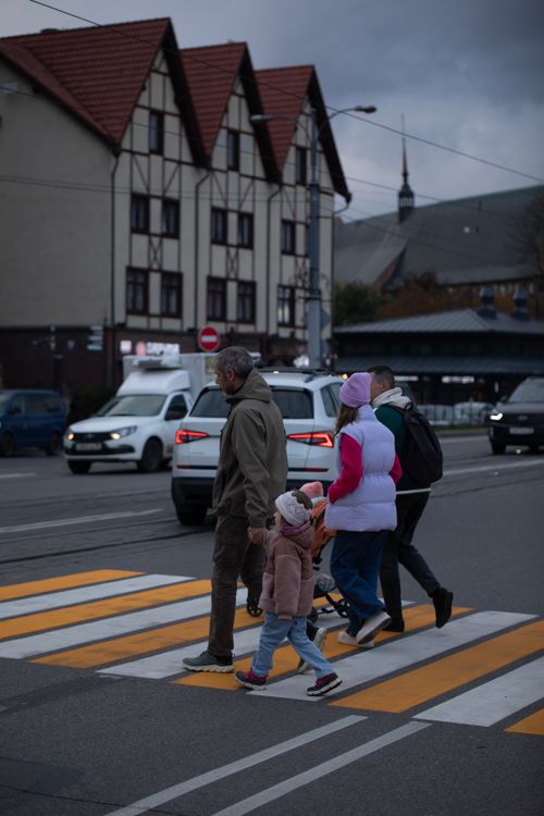Free A family crosses a street at dusk in an urban area with vehicles and buildings. Stock Photo