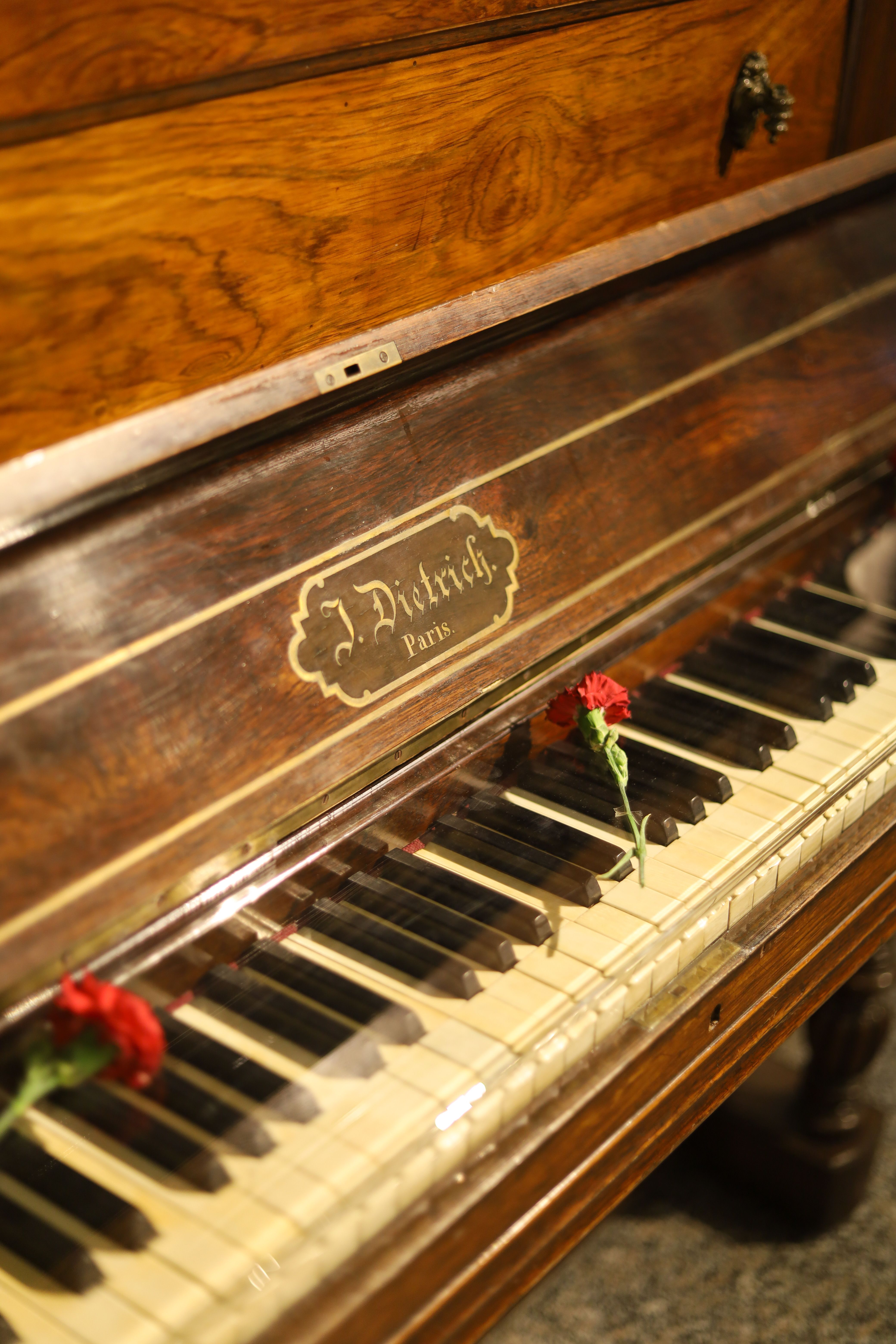 Close-up of a vintage J. Dietrich piano with red carnations on the keys.