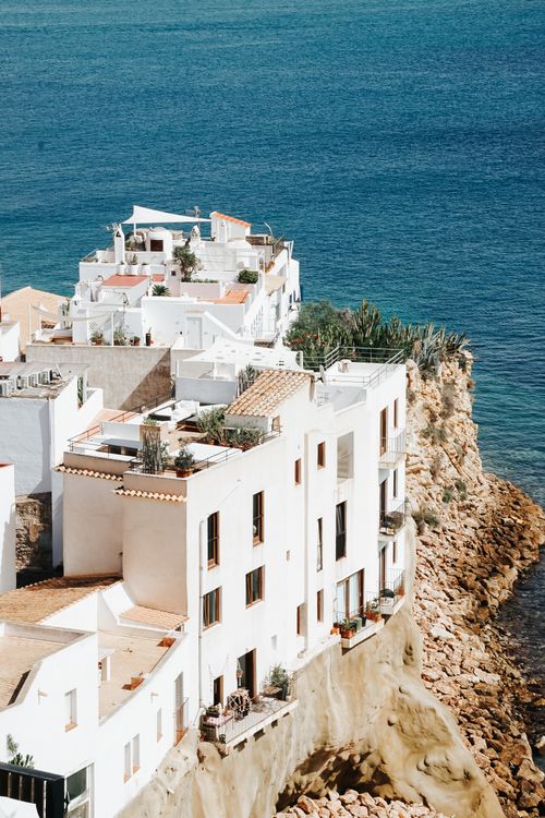 Free Picturesque white houses on a rocky cliff against a clear blue sea backdrop, ideal for travel and architecture themes. Stock Photo