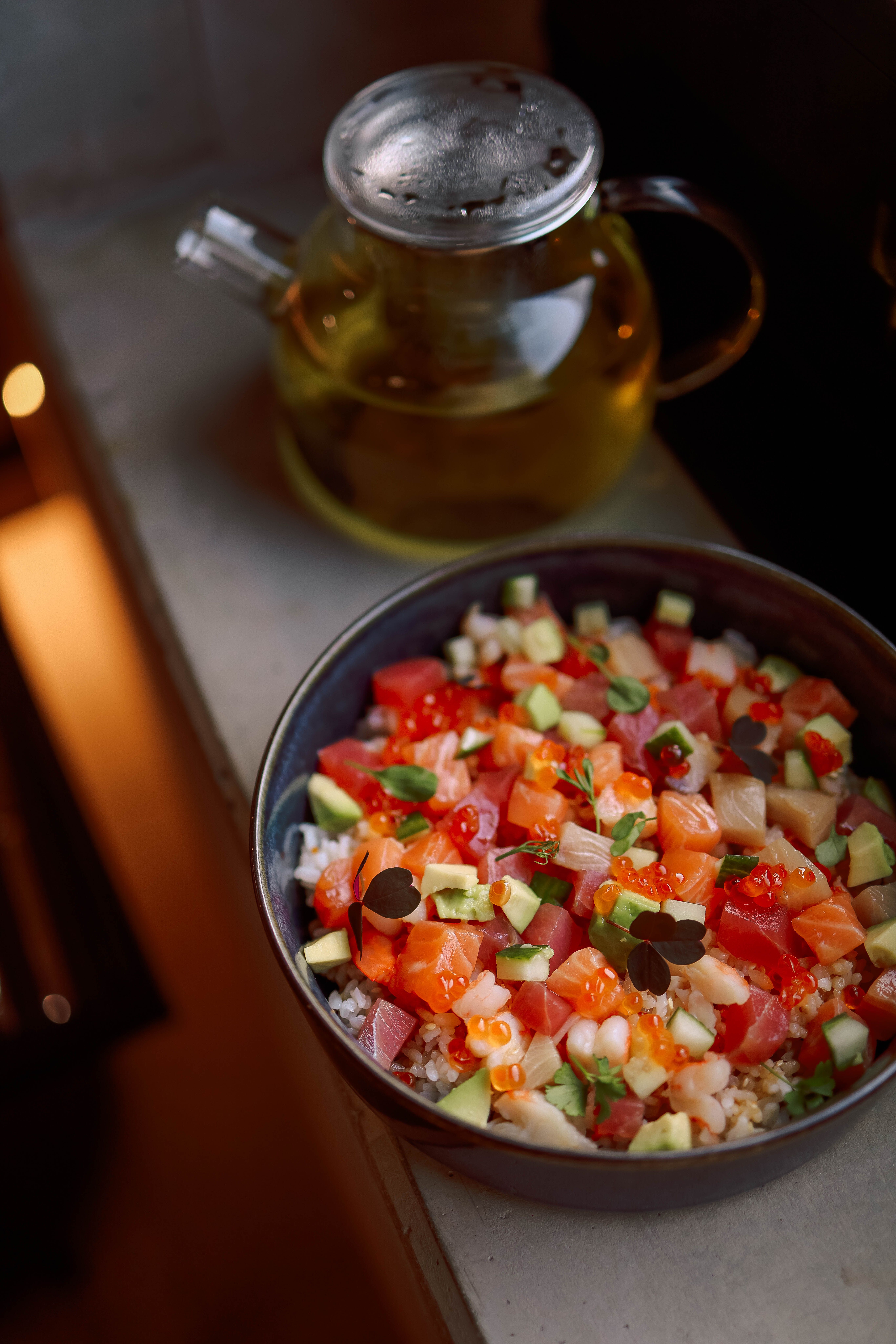 Colorful poke bowl with salmon, tuna, and fresh vegetables, accompanied by olive oil.