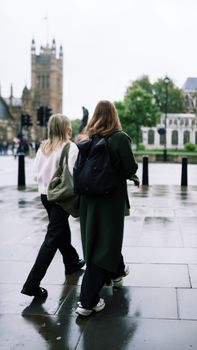 Two women walking along wet city streets near historic architecture.