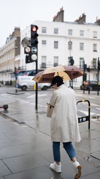 Elegant city scene with a person walking under an umbrella in rainy weather.