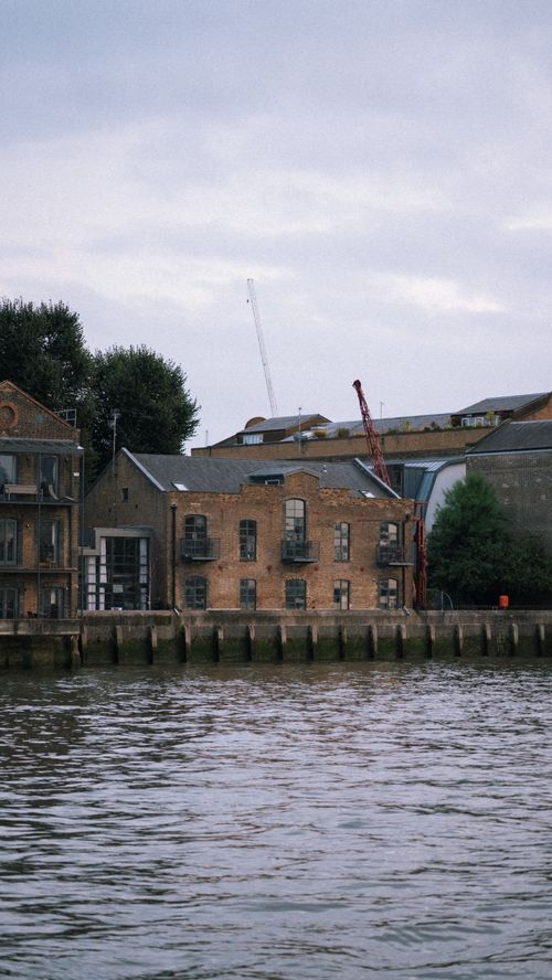 Free Serene riverside view of historic brick warehouses, reflecting an industrial charm. Stock Photo