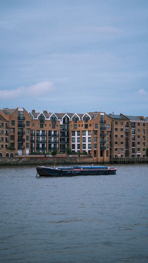 Free A vintage boat in front of charming riverside buildings on a cloudy day. Stock Photo