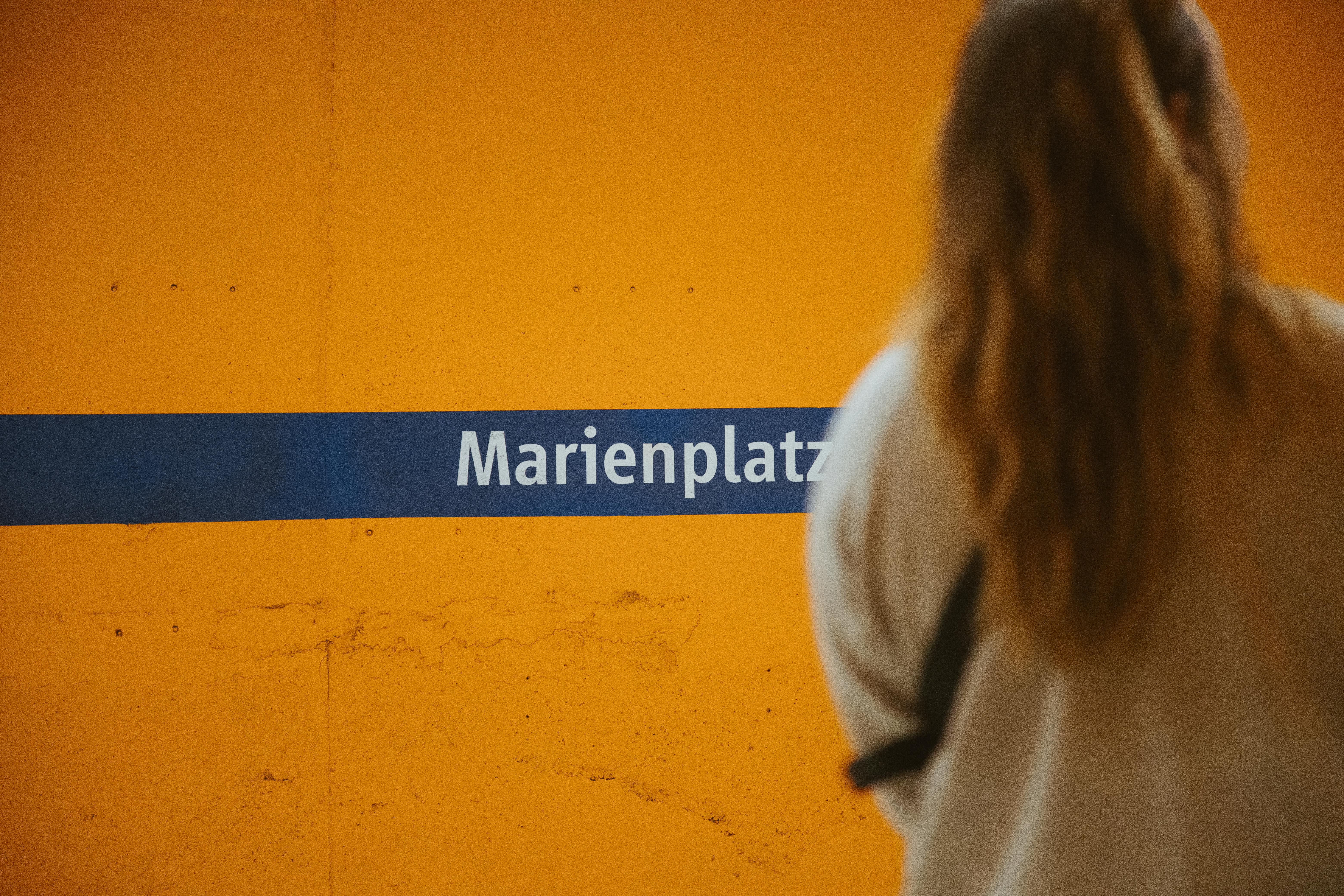 Woman at Marienplatz subway station in Munich, featuring yellow wall and sign.