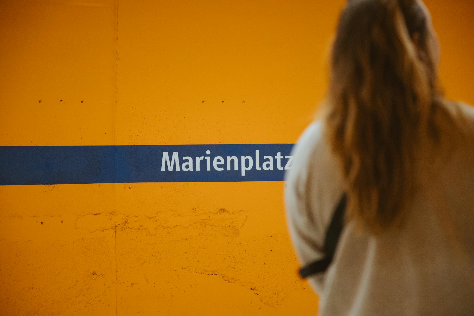 Woman at Marienplatz subway station in Munich, featuring yellow wall and sign.