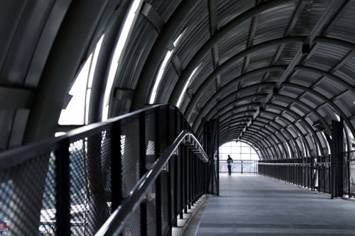 Free A person walks through a modern arched indoor pedestrian bridge with steel structure. Stock Photo