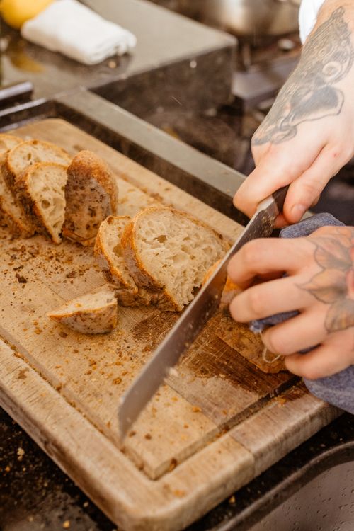 Free Close-up of hands slicing freshly baked artisan bread on a wooden cutting board in a modern kitchen. Stock Photo