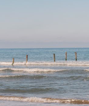 Gentle ocean waves lapping against old wooden posts under a clear sky, embracing tranquility.