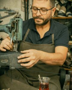 Experienced cobbler fixing shoe using sewing machine with tea in foreground.