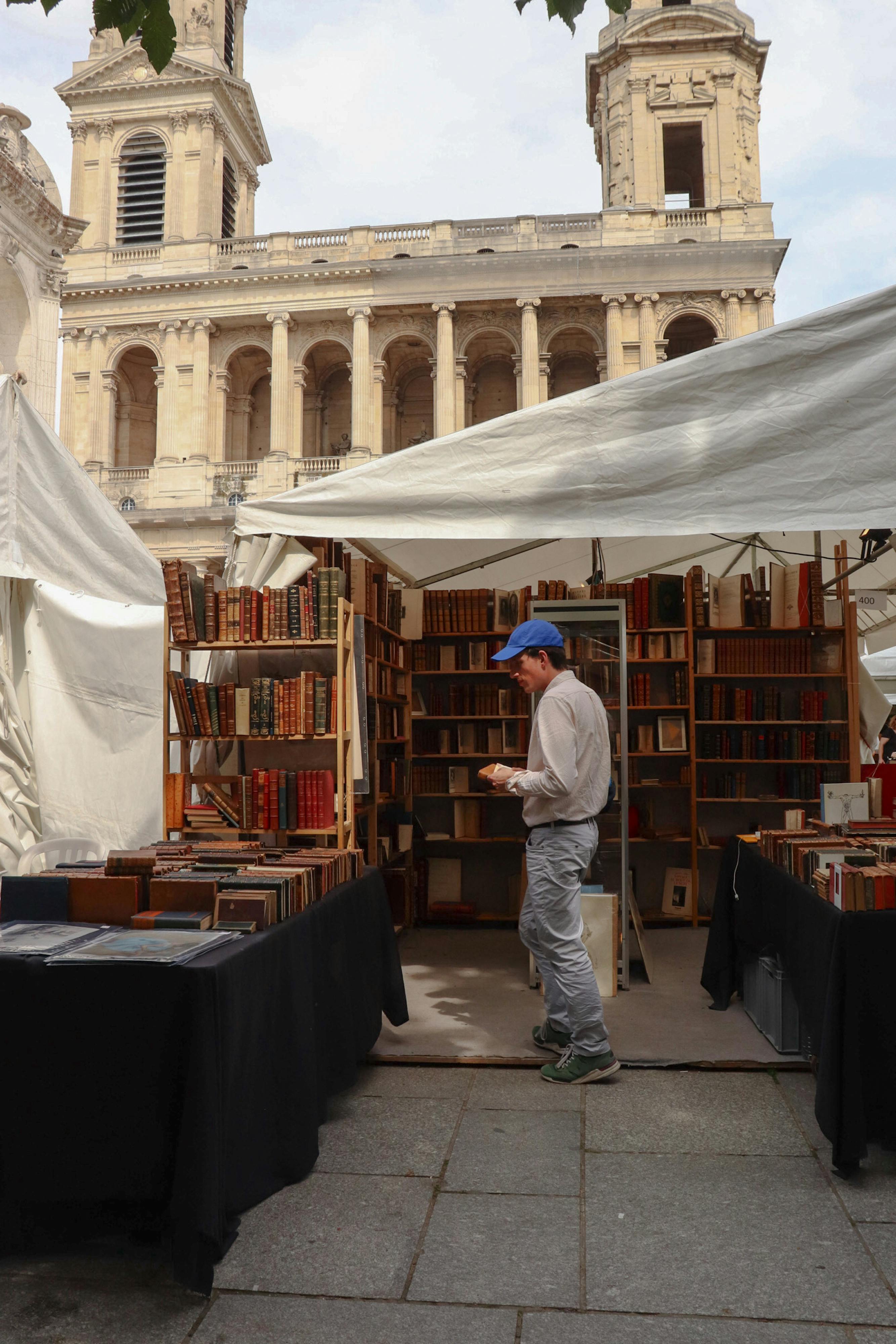 Man browsing books at outdoor bookstall near Saint-Sulpice Church, Paris.