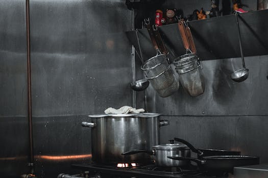 Stainless steel commercial kitchen setup with pots, strainers, and utensils hanging on a rail.