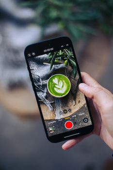 Top view of a matcha latte with art captured on a smartphone outdoors.