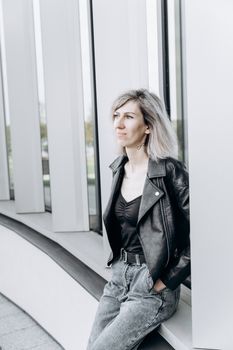 Stylish woman in a black leather jacket leaning against a modern architecture indoors.