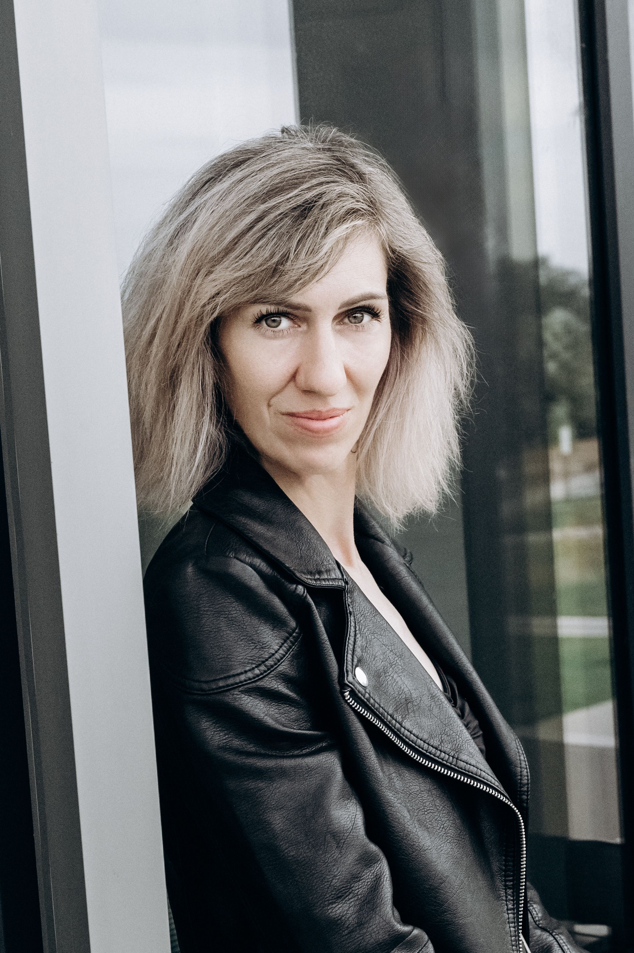 Confident woman posing in a black leather jacket outdoors.