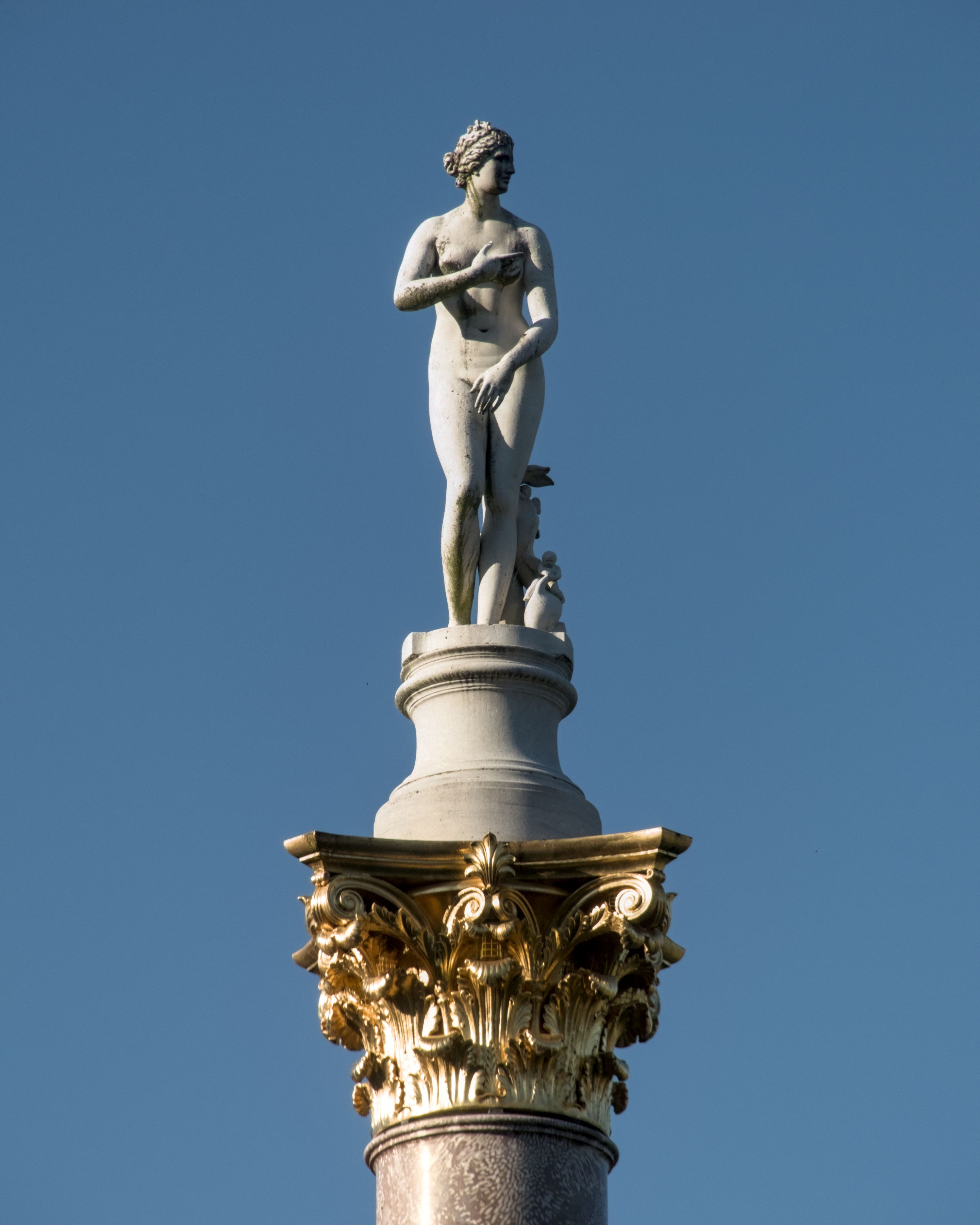 Classical statue of a nude woman atop ornate column against clear blue sky in Potsdam, Germany.