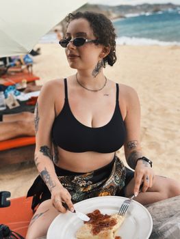 Woman in swimwear enjoys a crepe at a sunny beach. Relaxation and summer vibes.