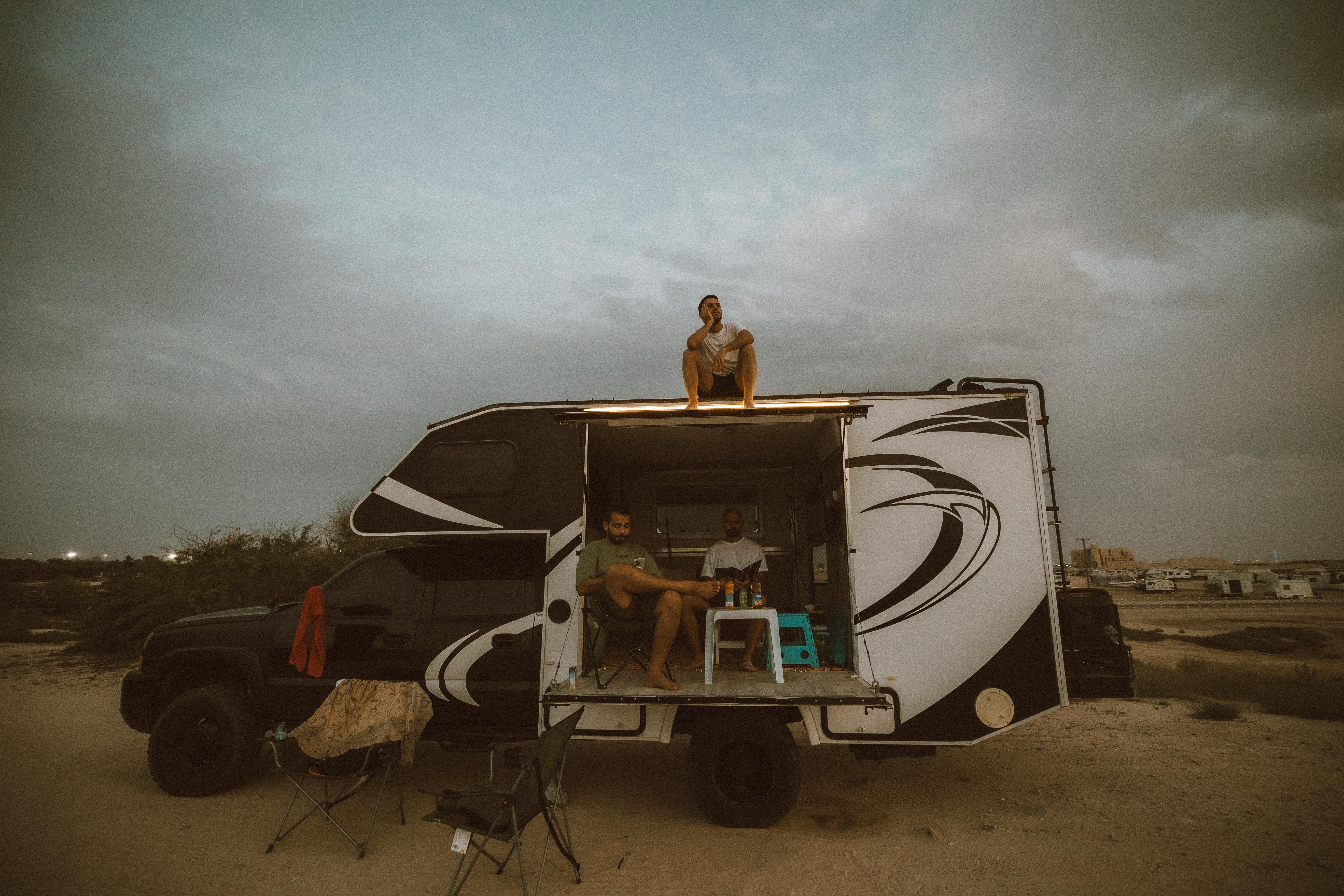 Free Three friends enjoying a camping trip in Dubai's desert, relaxing near a camper van. Stock Photo