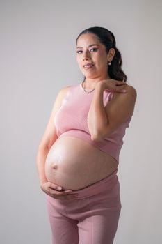 A pregnant woman smiling and posing in pink clothing on a neutral background. - Fotografer Sidoarjo