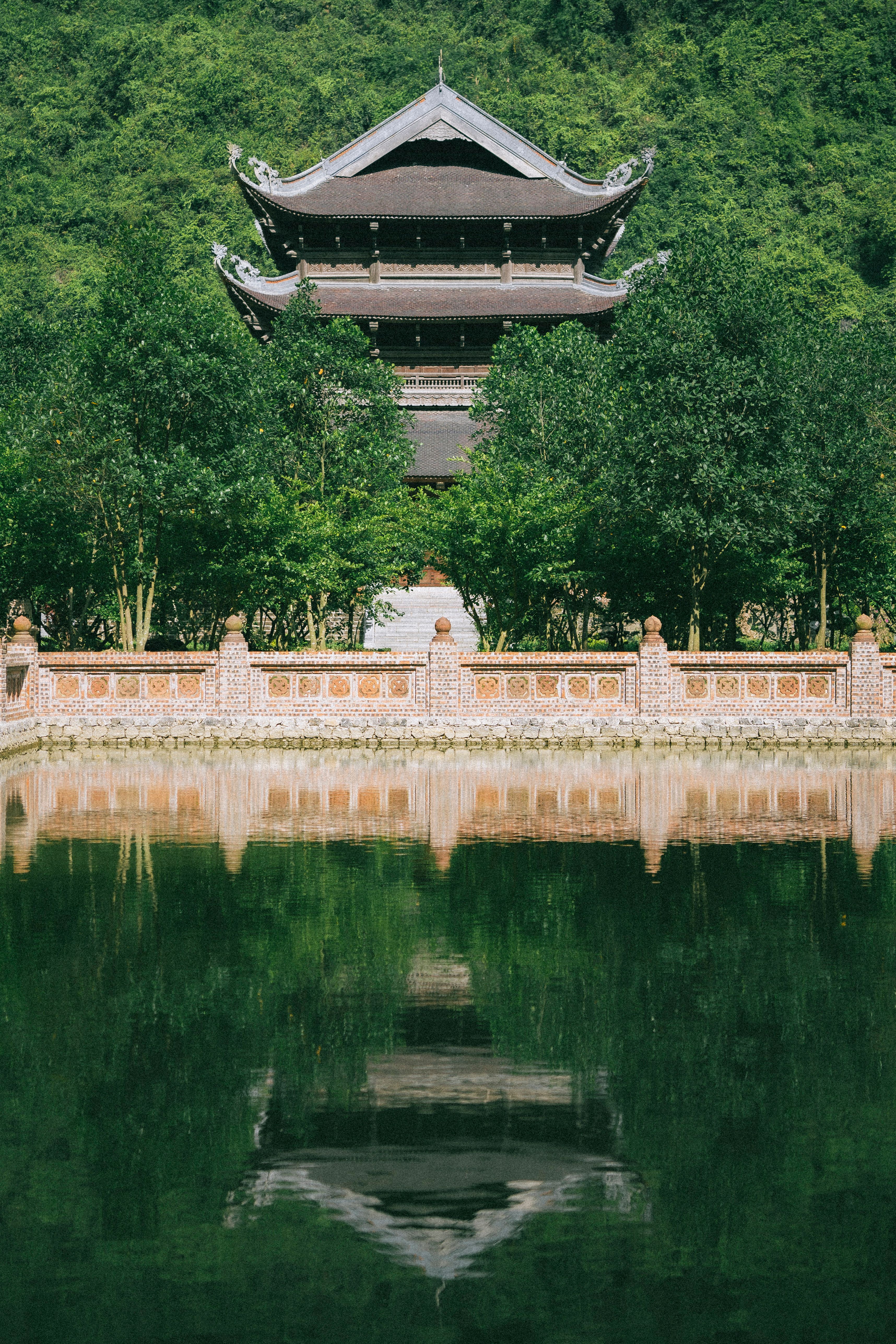 A serene view of a pagoda reflected in water, surrounded by lush greenery in Ninh Bình, Vietnam.