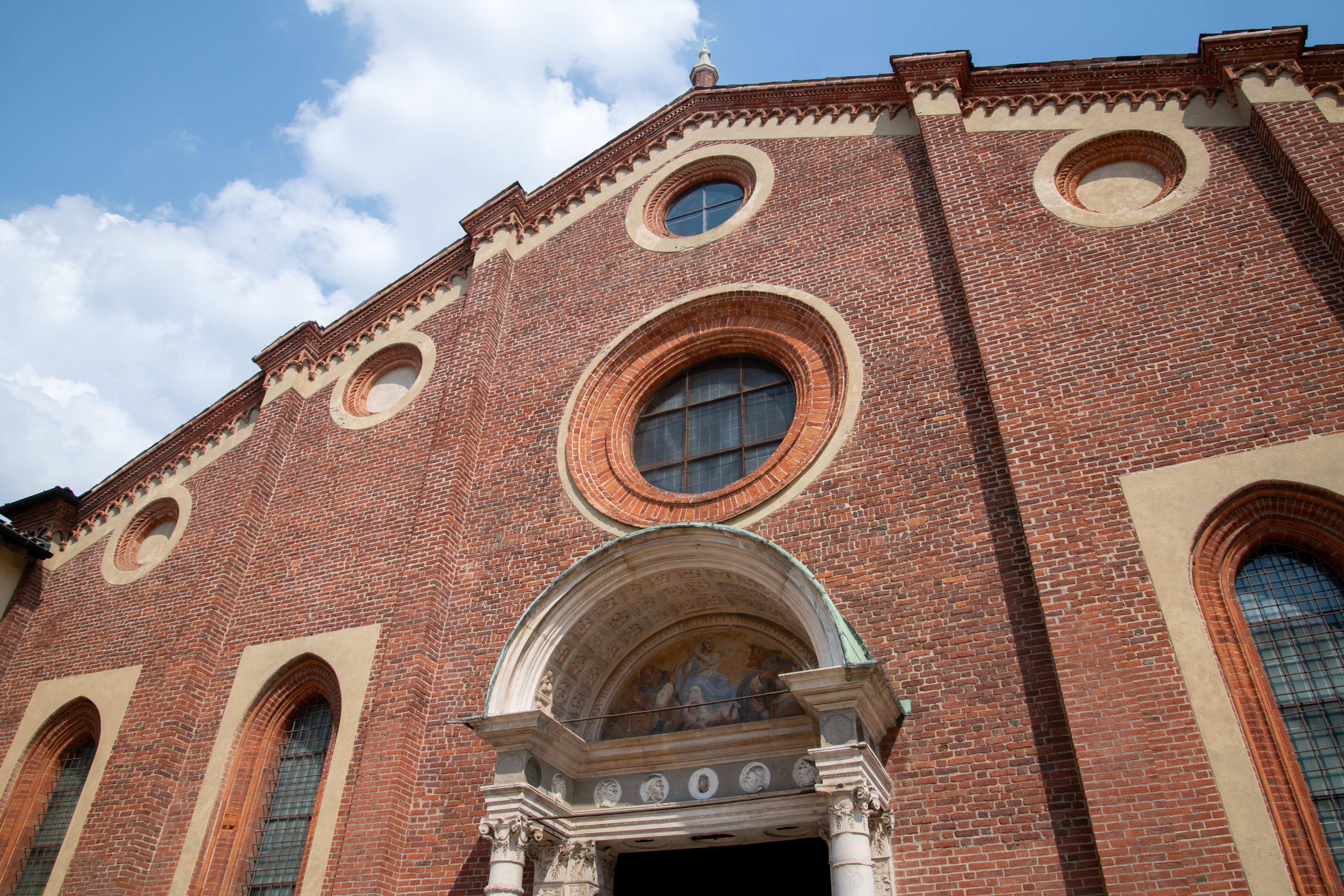 Fachada de tijolos vermelhos da Igreja de Santa Maria delle Grazie em Milão, Itália, vista sob luz brilhante e céu azul, sem pessoas visíveis