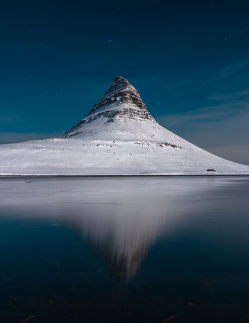 Majestic night view of snow-capped Kirkjufell Mountain with water reflection in Iceland.