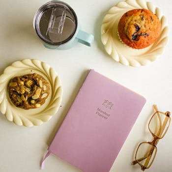 Flat lay featuring coffee, muffin, cookie, and a planner on a table.