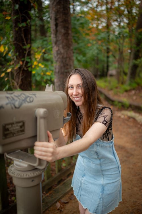 Free Smiling woman interacts with a viewfinder in a lush autumn forest setting. Stock Photo