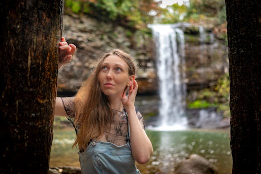 Young woman in denim posing by a stunning waterfall surrounded by nature.