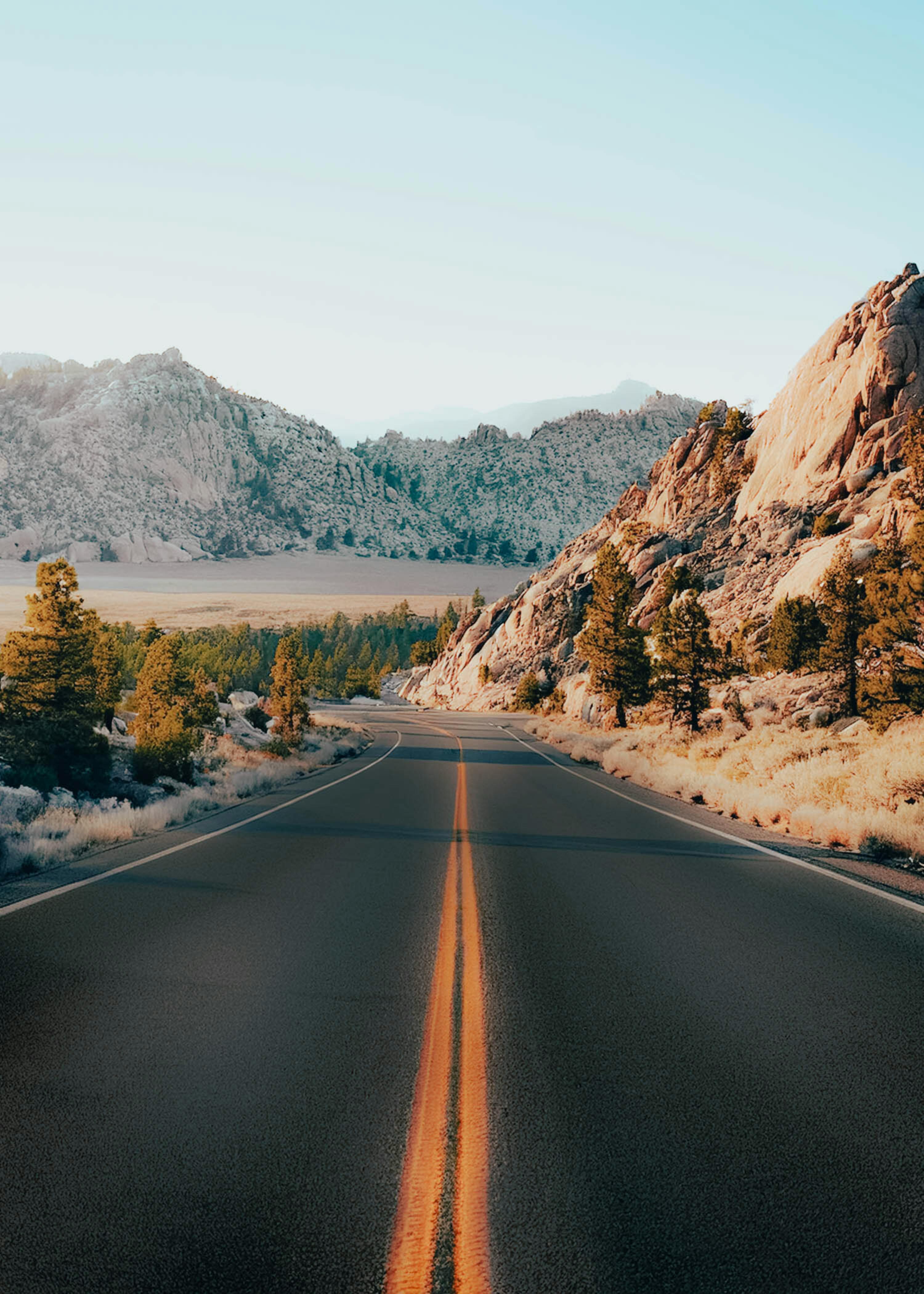 Discover a stunning view of a deserted road cutting through rocky desert terrain under clear blue skies.