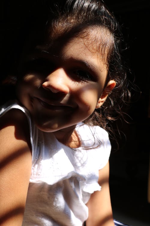 Adorable little kid smiling and looking at camera through bright sunlight rays