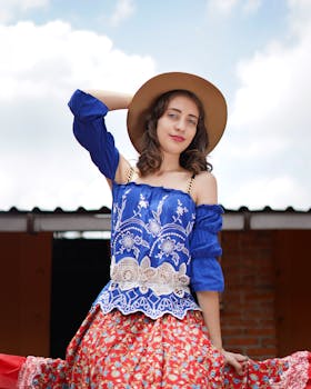 Boho chic woman in vibrant blue top and floral skirt posing outdoors with a hat.