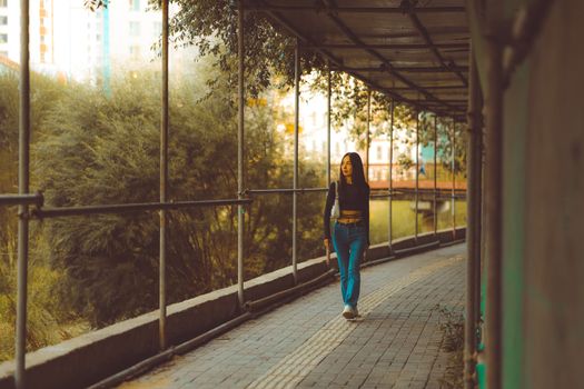A young woman walking along a covered urban pathway surrounded by greenery.