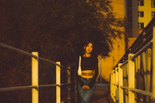 Free Stylish young woman standing on a bridge bathed in golden hour light, exuding urban charm. Stock Photo