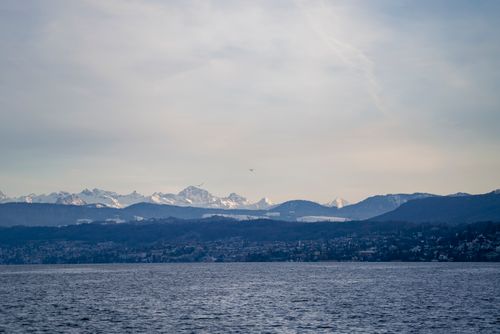 Free A serene view of snow-capped Swiss Alps with Lake Zurich in the foreground under a clear sky. Stock Photo