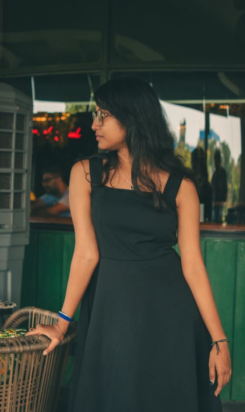 Free A stylish woman standing indoors, wearing glasses and a black dress, exuding a casual and relaxed vibe. Stock Photo