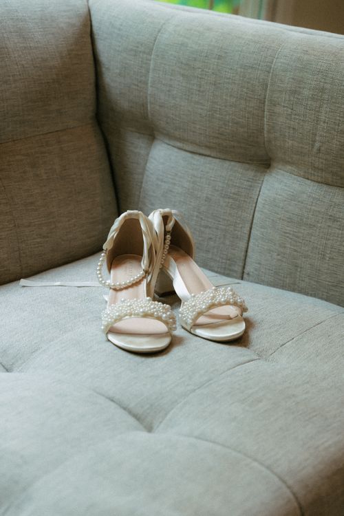 Free Delicate bridal shoes adorned with pearls resting on a sofa, perfect for a wedding day. Stock Photo