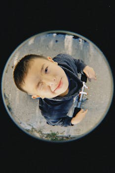 A young boy winks playfully at the camera while holding a toy, captured with a fisheye lens.