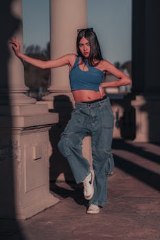 Stylish young woman in casual jeans and top posing confidently by pillars outdoors.
