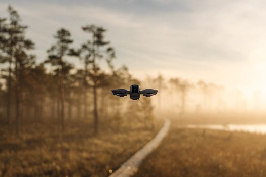 A drone hovers over a misty forest path during sunrise, capturing nature's beauty.