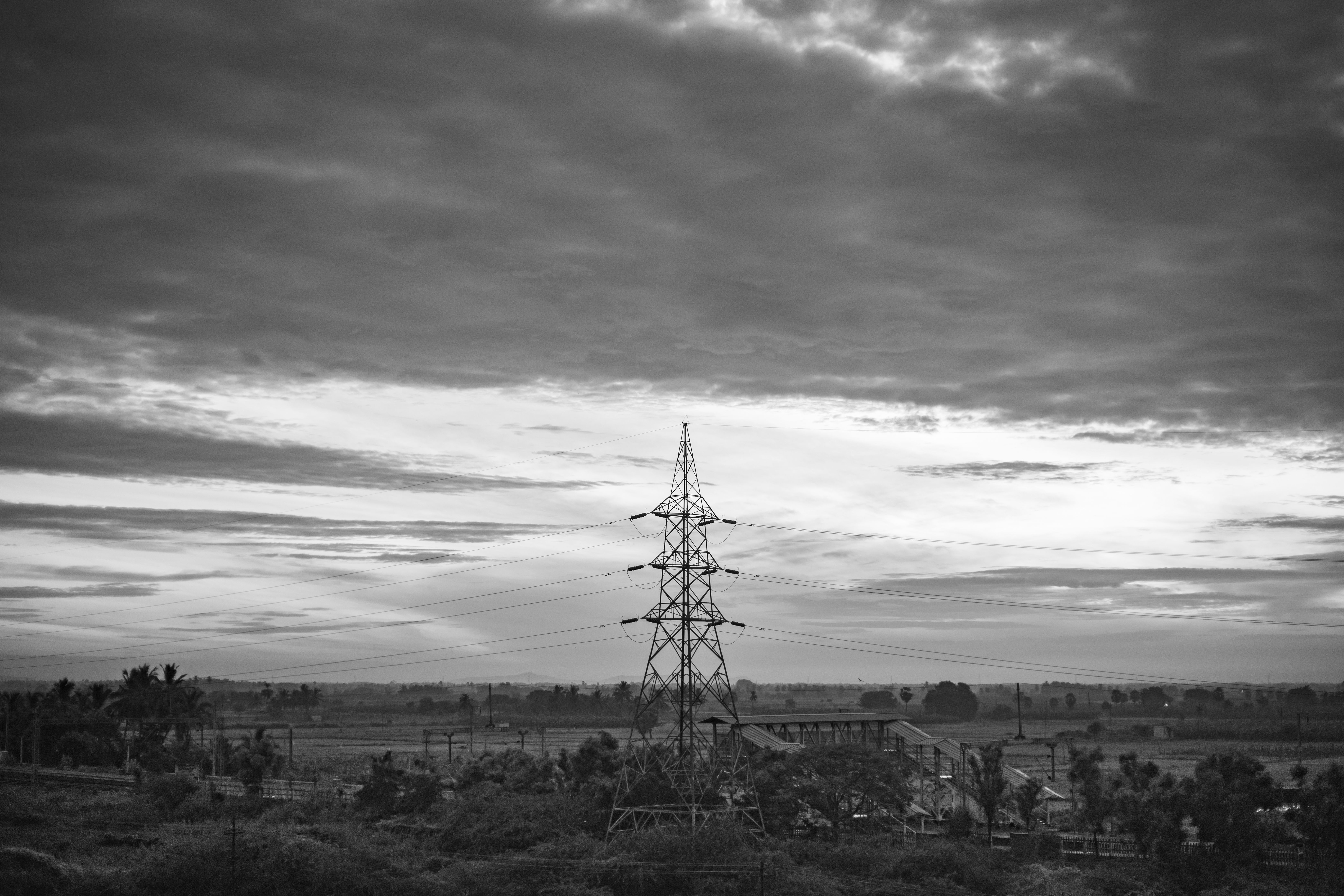 Monochrome rural landscape featuring transmission tower and clouds in Nanguneri, India.