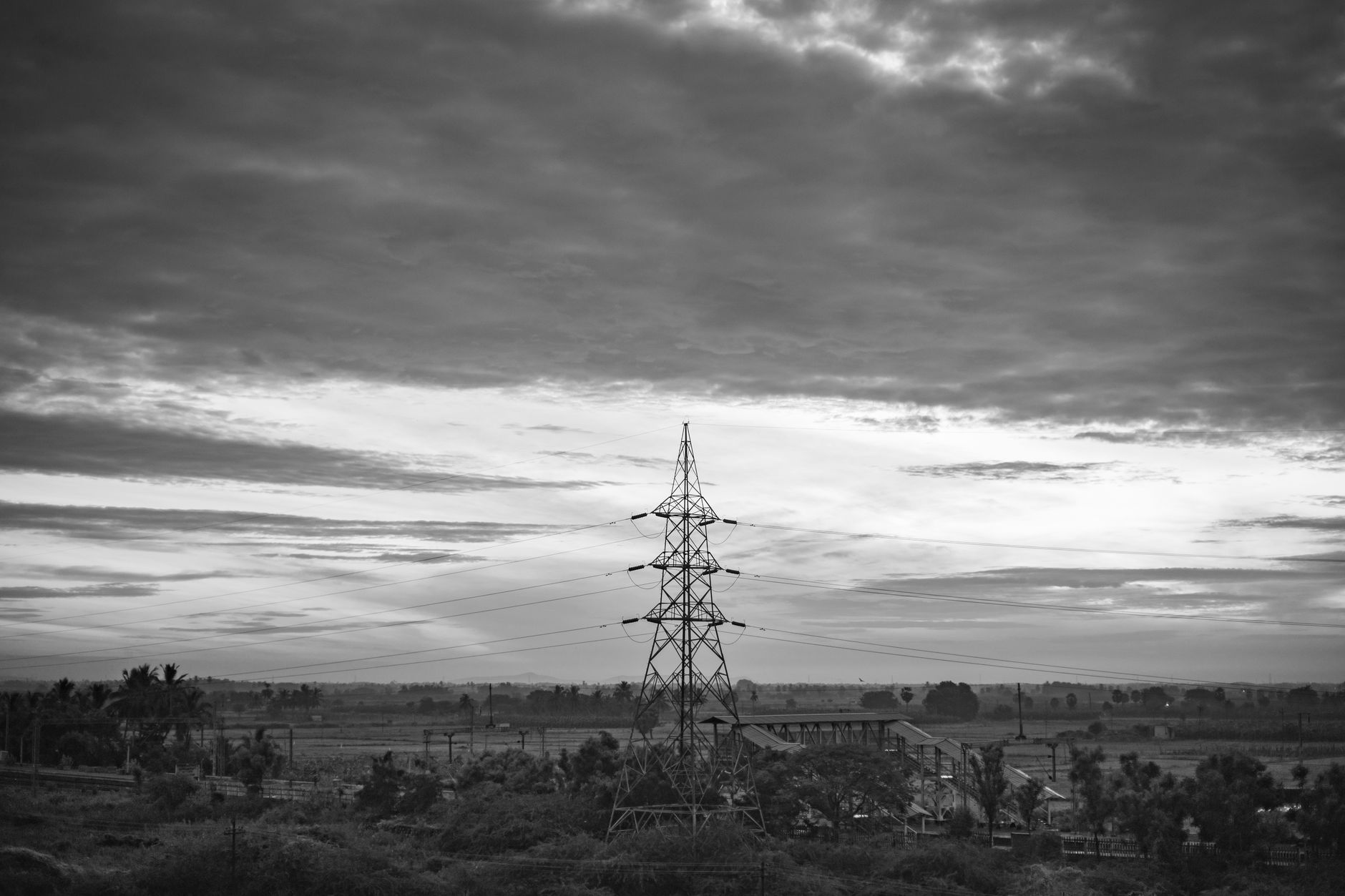 Monochrome rural landscape featuring transmission tower and clouds in Nanguneri, India.