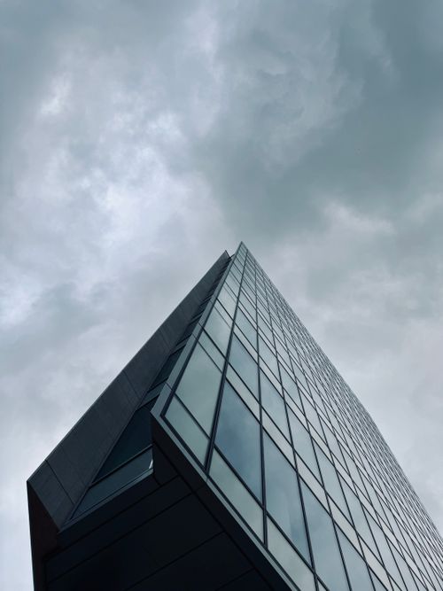 Free Low-angle view of a sleek skyscraper with reflective glass under a cloudy sky. Stock Photo