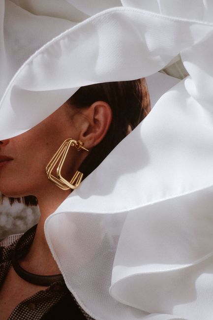 Close-up of a woman with a gold earring, partially covered by flowing white fabric.
