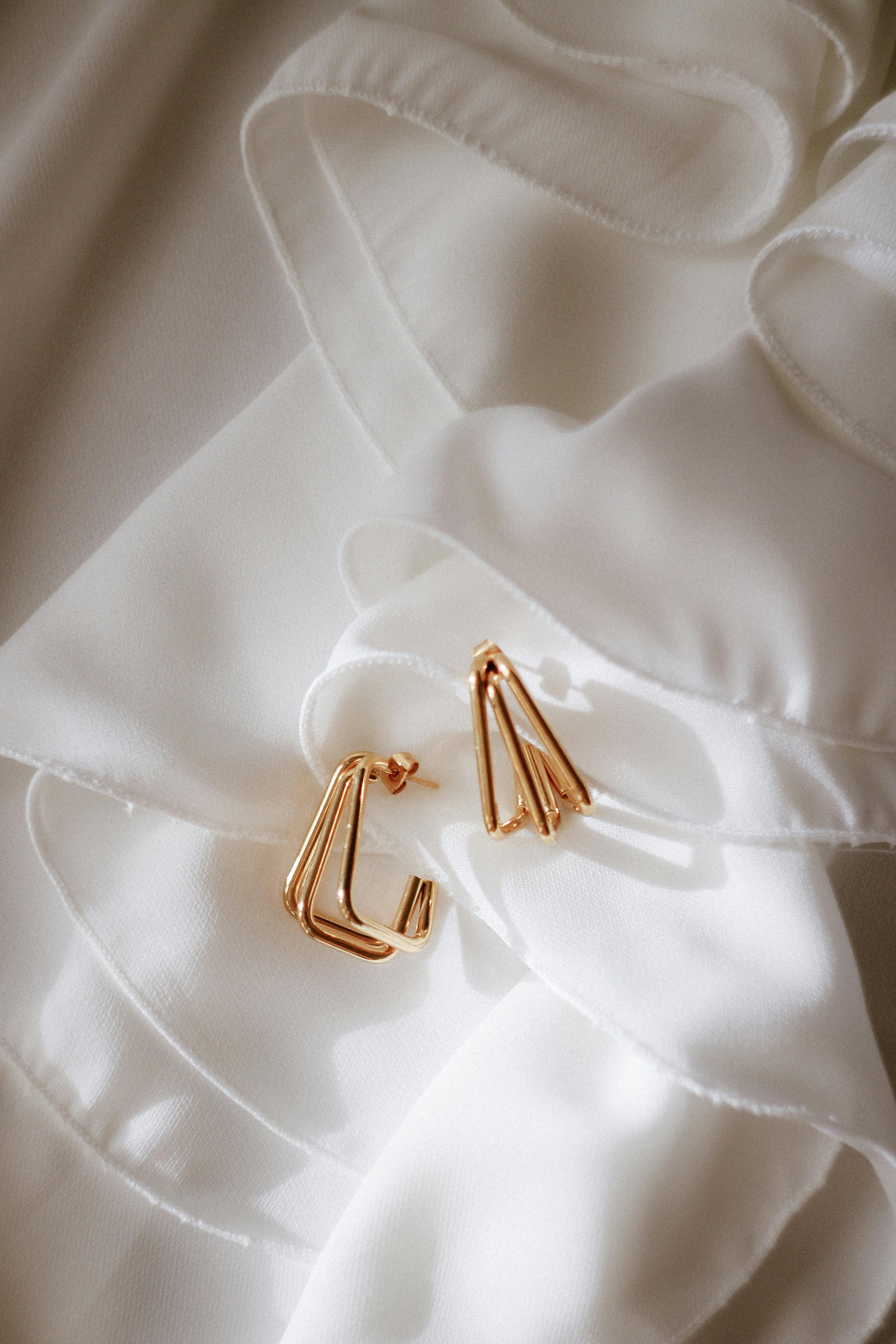 Close-up of gold earrings elegantly placed on luxurious white silk fabric.