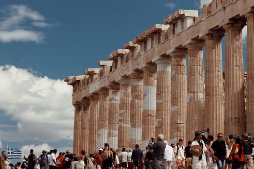 A lively scene with tourists exploring the iconic Parthenon in Athens, Greece, under a clear blue sky.